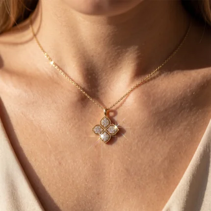 Gold chain necklace with a four-leaf clover pendant encrusted with small diamonds resting on a model's collarbone.