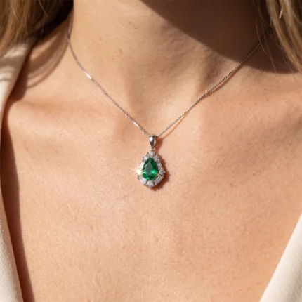 Teardrop emerald pendant surrounded by diamonds on a silver chain resting on a woman's collarbone, close-up.