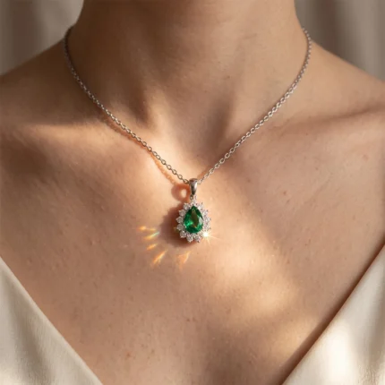 Emerald teardrop pendant surrounded by diamonds on a silver chain resting on the collarbone.