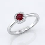 Silver ring with a round red ruby centerpiece surrounded by a halo of small diamonds on a polished band, brand name inside.