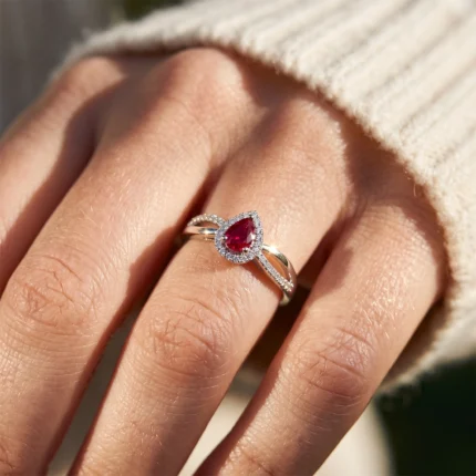 Close-up of a hand wearing a pear-shaped ruby ring with a diamond halo and pavé-set band on a gold ring.