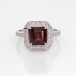 White gold ring featuring a large square-cut deep red center stone, surrounded by pink diamonds in an octagonal setting with a pavé diamond band