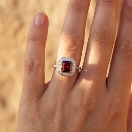 Close-up of a hand wearing a silver ring with a square red ruby surrounded by a diamond halo.