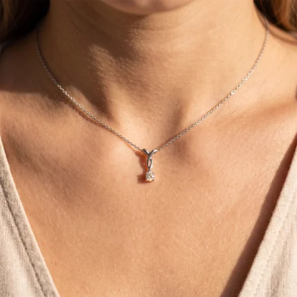 Close-up of a silver necklace with a twisting loop pendant and small gemstone, resting on a tan neckline.