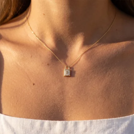 Gold necklace with a small square gold padlock pendant resting on a woman's décolletage.