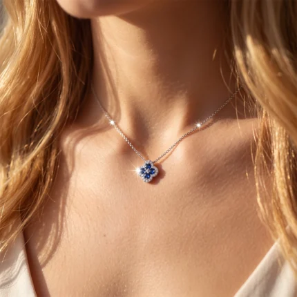 Silver chain necklace with a blue four-petaled flower pendant resting on a woman’s décolletage in sunlight.
