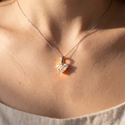 Heart-shaped diamond pendant on a delicate silver chain resting on the neckline of a person.