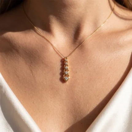 Gold necklace with a vertical row of diamond-studded links resting on a woman's décolletage, forming a leaf-like pendant's shape.