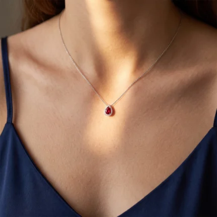 Teardrop ruby pendant necklace on a woman’s neck, silver chain with a halo of small diamonds.