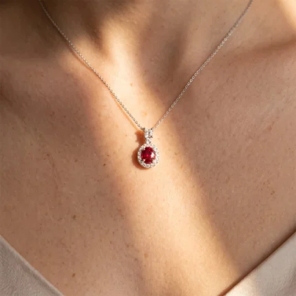 Pendant necklace with a red gemstone surrounded by small diamonds on a silver chain resting on the neck.