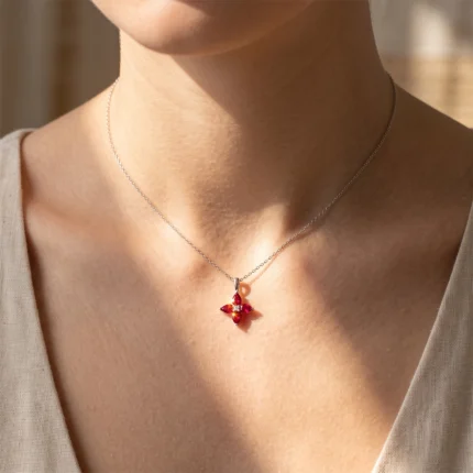 Close-up of a silver chain necklace with a red gemstone cross pendant resting on the collarbone.