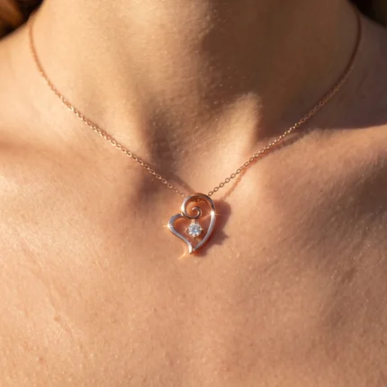 Rose gold heart-shaped pendant necklace with a single diamond on a delicate chain around the neck.
