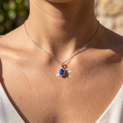 Silver chain necklace with a blue oval gemstone pendant surrounded by small diamonds on a sunlit neckline.