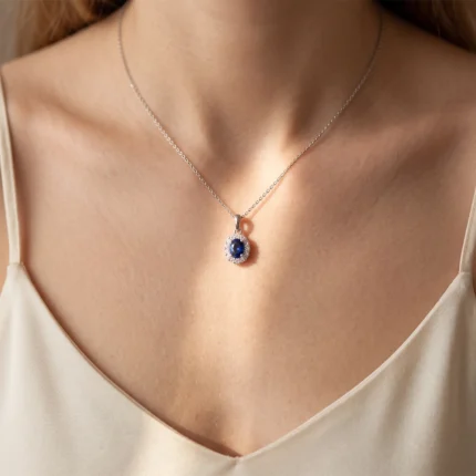 Silver chain necklace with an oval blue gemstone pendant surrounded by small diamonds resting on a woman’s décolletage.