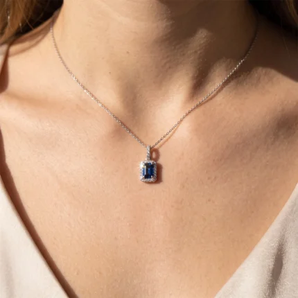 Silver chain necklace with a rectangular blue gemstone pendant surrounded by small diamonds, resting on the collarbone.
