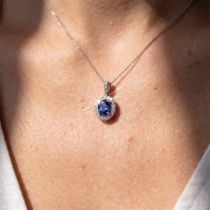 Silver chain necklace with an oval blue gemstone pendant surrounded by a halo of diamonds on a woman's chest.