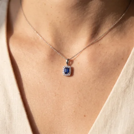 Silver chain necklace with a square blue gemstone pendant surrounded by tiny diamonds on a skin-toned neckline