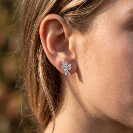 Close-up of a woman's ear with a sparkling diamond flower earring on the earlobe, in sunlight.