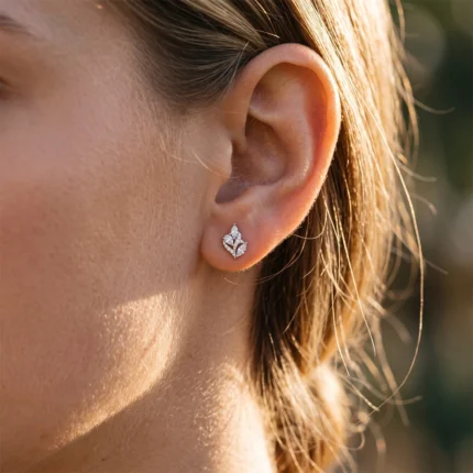 Close-up of an earlobe with a diamond-studded leaf-shaped earring in sunlight