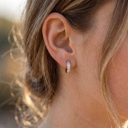 Close-up of a woman's ear wearing a small silver hoop earring with stones.