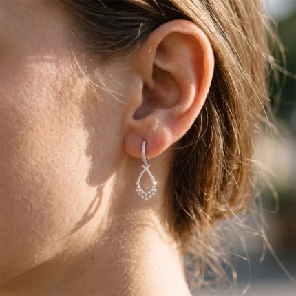 Close-up of a woman's ear with a dangling diamond teardrop earring catching sunlight on its stones.