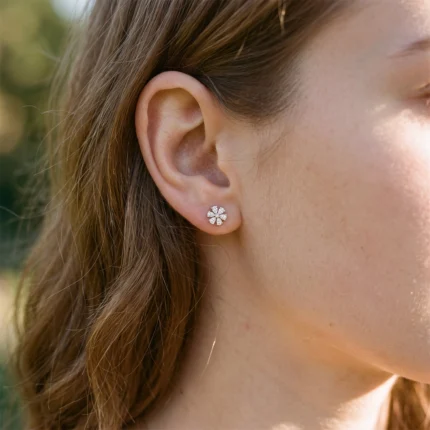 Close-up of a woman's ear wearing a small diamond flower stud earring in sunlight.