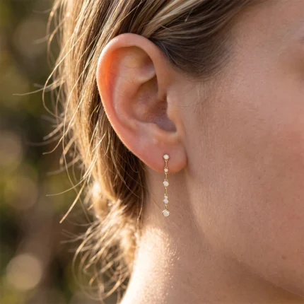 Close-up of a ear with a long gold dangle earring featuring small round stones.