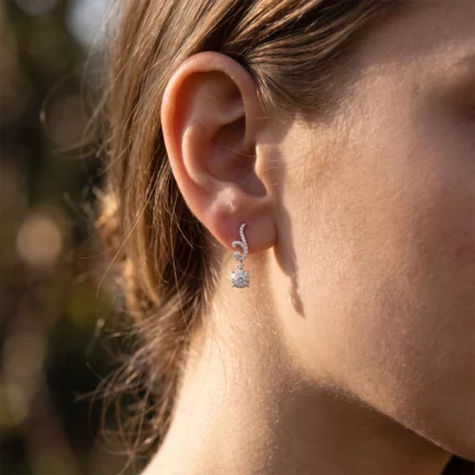 Close-up of a woman's ear wearing a dangling diamond earring outdoors.