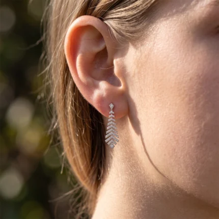 Close-up of a woman's ear wearing a silver diamond-studded drop earring with leaf-shaped links.