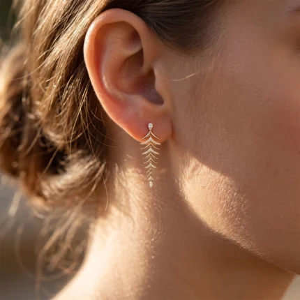 Close-up of a woman's ear wearing a gold, leaf-shaped drop earring with diamond accents.