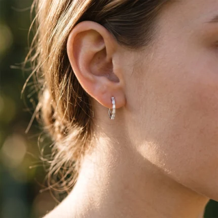 Close-up of a woman's ear with a small silver hoop earring encrusted with stones in sunlight