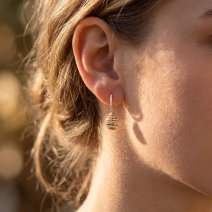 Close-up of a woman's ear wearing a gold hoop with a drop, diamond-studded, segmented pendant.