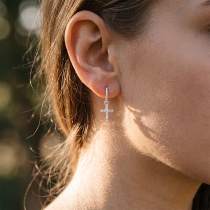 Close-up of a woman's ear wearing a silver diamond-studded cross drop earring.