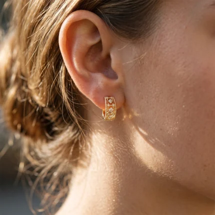 Gold hoop earring with an intricate cutout pattern and small diamonds on the ear.