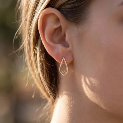 Close-up of a woman's ear wearing a gold teardrop-shaped earring outlined with small diamonds.