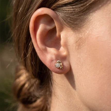 Close-up of a woman's ear with a gold bee-shaped stud earring encrusted with tiny diamonds on the earlobe.