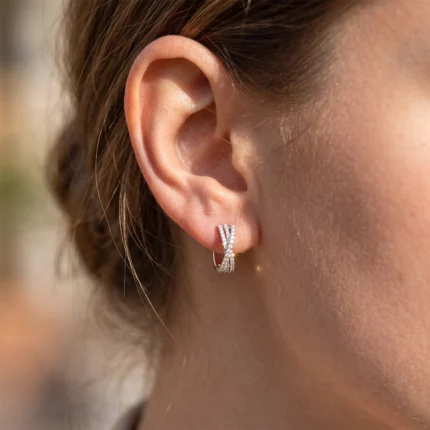 Close-up of a silver diamond hoop earring with a crisscross design on the earlobe.