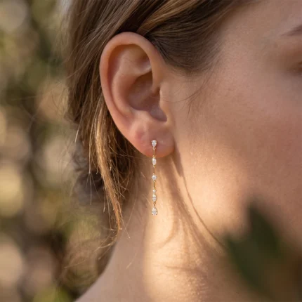 Close-up of a woman's ear wearing a gold drop earring with a vertical line of diamonds.