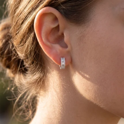 Close-up of a woman's ear with a diamond-studded hoop earring, in bright outdoor light.