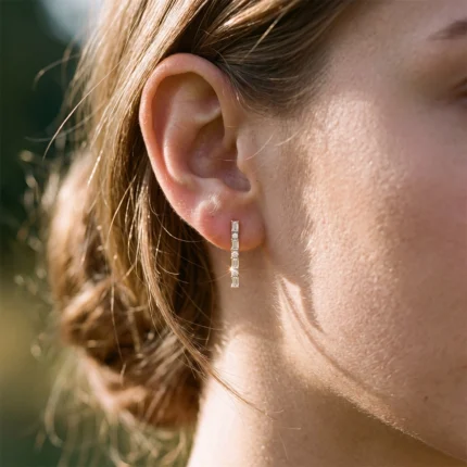 Close-up of a woman's ear with a vertical earring featuring four square diamonds in a row, catching the sunlight.
