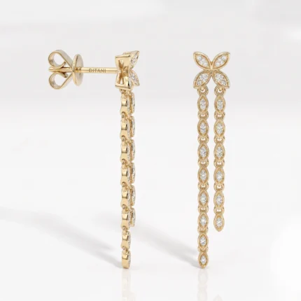 Gold drop earrings: left piece is a bow‑shaped stud, right piece is a long diamond‑paved chain with a four‑petal flower top and linked teardrop segments.