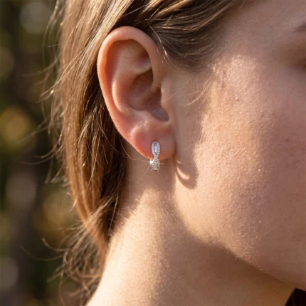 Close-up of a woman's ear wearing a small diamond-studded hoop earring with a teardrop design on a sunlit background.