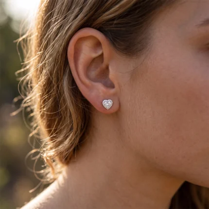 Heart-shaped diamond stud earring on a woman's earlobe with a halo of small stones