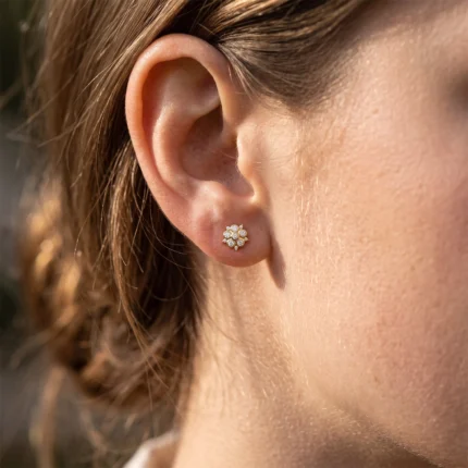 Close-up of a woman's ear with a small gold flower-shaped diamond stud earring on the earlobe.