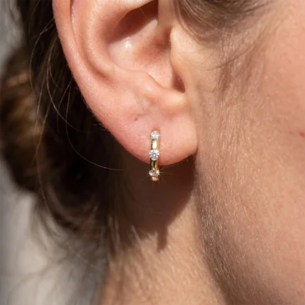Close-up of a gold hoop earring with three small diamonds on the earlobebar pierced ear.