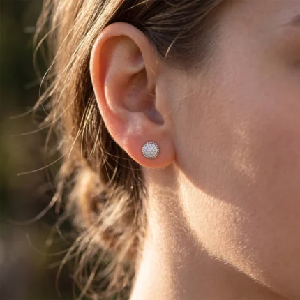 Close-up of a woman's ear with a round pavé diamond stud earring on the earlobe.
