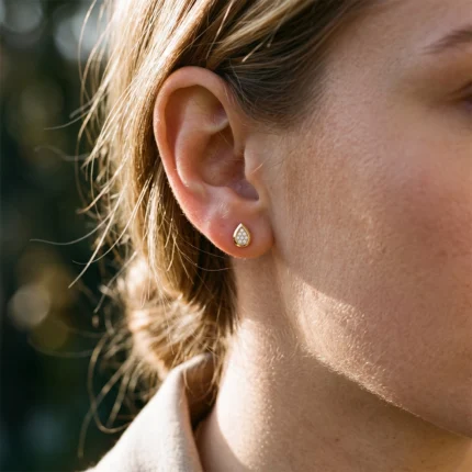 Close-up of a woman's ear wearing a small teardrop gold stud with diamond accents.