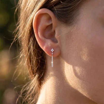 Close-up of an ear wearing a diamond-stud and dangling diamond bar earring in sunlight.