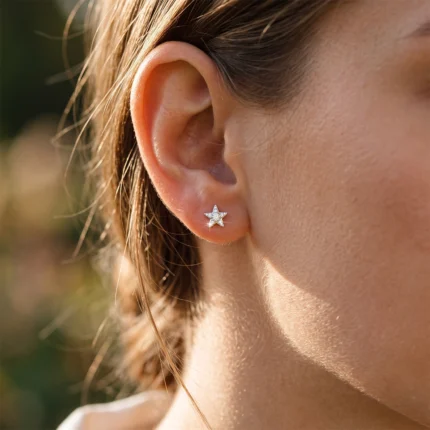 Close-up of a woman's ear wearing a small silver star-shaped stud earring with a sparkly center.