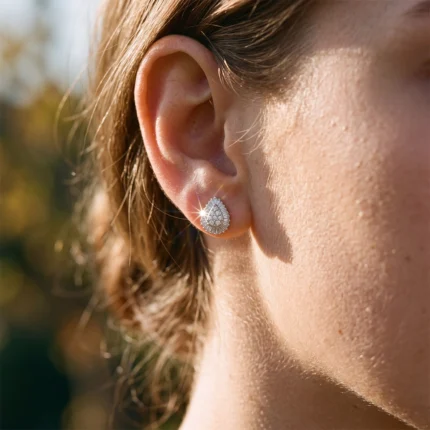 Close-up of a woman's ear with a teardrop-shaped diamond earring catching sunlight.